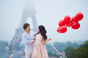 Beautiful romantic couple in love with bunch of red balloons together near the Eiffel tower in Paris on a cloudy and foggy rainy day