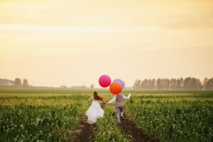Wedding couple running away on the field with big bright colored balloons, full body
