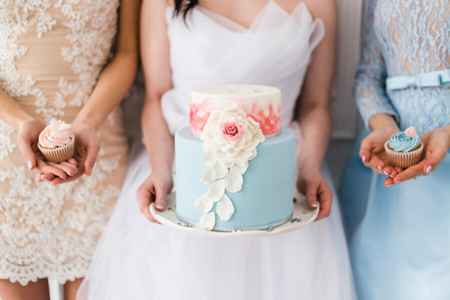 Bride in wedding dress holding a beautiful blue wedding cake, bridesmaids hollding cupcackes
