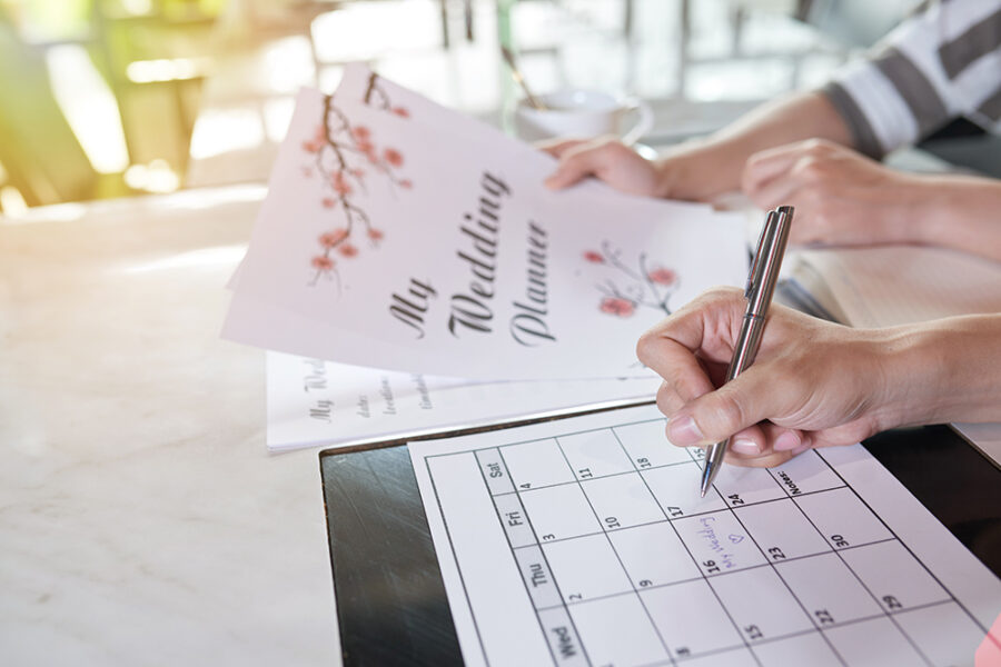 Young couple planning wedding day together and taking necessary notes in calendar while sitting at home, close-up shot