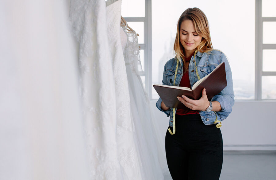 Female tailor writing in a diary while standing wedding dress store. Female dress designer working in bridal clothing store.