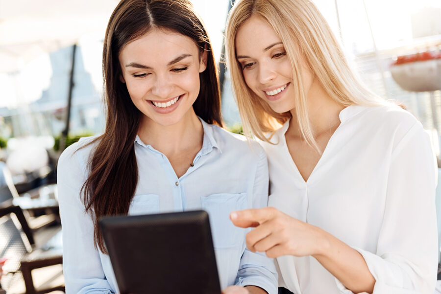 Modern electronic device. Happy positive female colleagues smiling and using a tablet while working together
