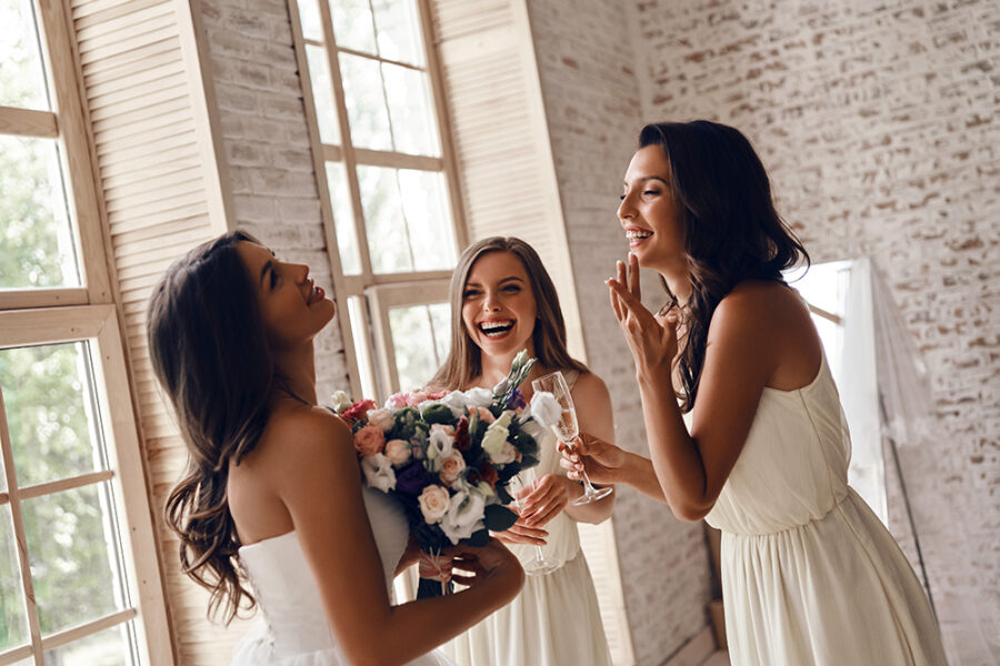 Attractive young woman holding a wedding bouquet and smiling while her girlfriends drinking champagne