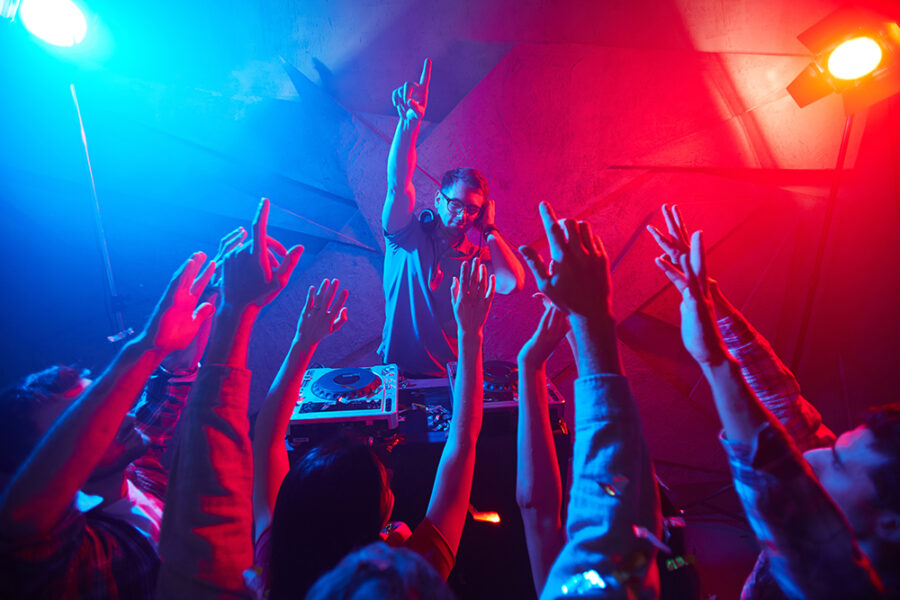 Deejay in headphones raising his hand and enjoying disco with the crowd