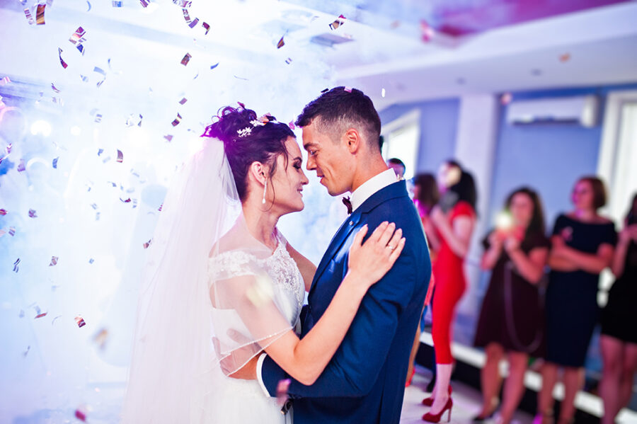 Touching and emotional first dance of the couple on their wedding with confetti and colorful lights on the background.