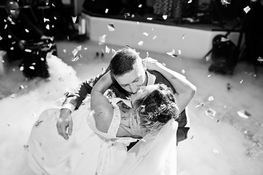 Newly married couple dancing on their wedding party with heavy smoke and multicolored lights on the background. Black and white photo.