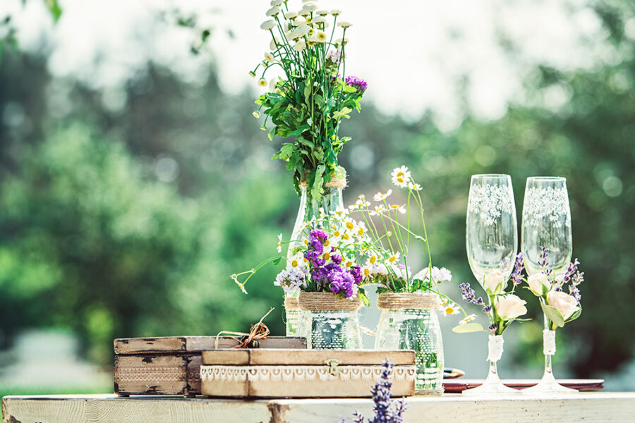 beautiful vintage wedding ceremony outdoors. Summertime. Old white wooden house. Tree decorated with white cages full of flowers. rustic style table with two glasses of cold champagne