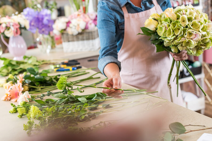 cropped shot of young florist in apron working with flowers and arranging bouquet