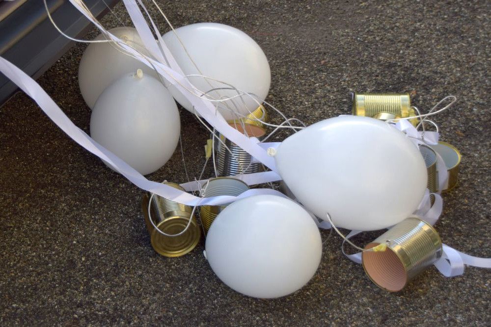 Auf dem Bürgersteig liegen weiße Luftballons und leere, mit Bändern zusammengebundene Blechdosen.