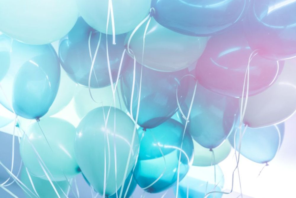 Eine Gruppe blauer und blaugrüner Luftballons mit weißen Schnüren schwebt vor einem hellen Hintergrund und erinnert an die verträumte, pastellfarbene Essenz von „heiraten im Frühling“. Weiches, diffuses Licht verstärkt den ätherischen Charme der Szene.