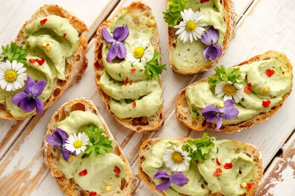 Leckere Canapes mit Avocadopaste und essbaren Blumen auf Holzuntergrund