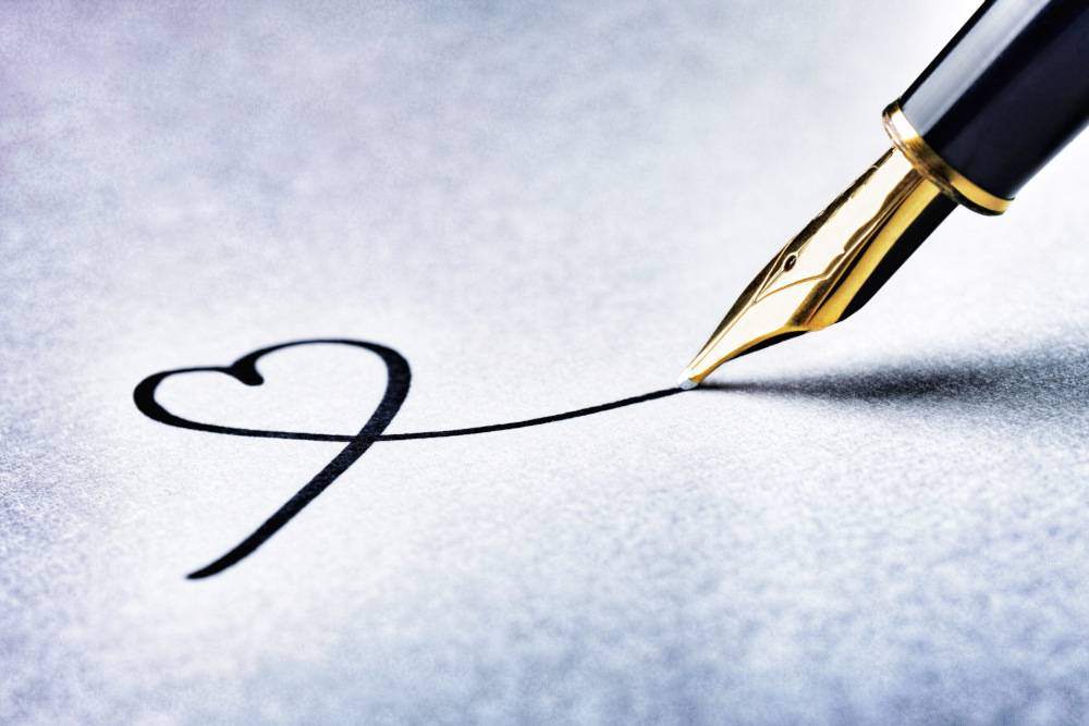 Nahaufnahme eines Füllfederhalters, der eine Herzform auf eine glatte, helle Oberfläche zeichnet. Die Feder des Stifts ist goldfarben und die Tinte ist schwarz, was einen Kontrast zum Hintergrund bildet.